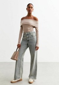 Beige topp utan axlar med långa ärmar, högmidjade ljusblå jeans, beige handväska, krämfärgade sneakers med brun detaljer.