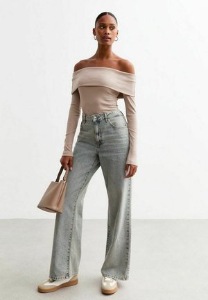 Top beige a spalle scoperte con maniche lunghe, jeans azzurri a vita alta, borsa beige, sneakers crema con accenti marroni.