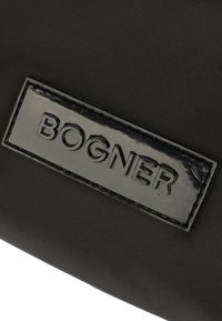 Black fabric bag featuring a glossy black leather patch with embossed "BOGNER" logo. Smooth texture and minimalist design.
