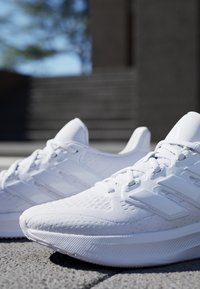 Witte sportieve schoenen met een gestructureerde mesh bovenkant en drie kenmerkende strepen. Beschikt over een slank ontwerp, ronde neus en een gevoerde zool.