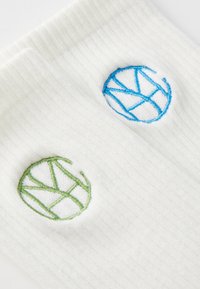 Chaussettes blanches côtelées avec des logos de cercles brodés en bleu et vert. Le logo bleu présente un design géométrique, tandis que le vert est similaire dans le style.