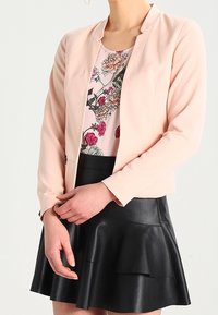 Ljusrosa blazer med en figurnära design, bärs över en blommönstrad topp. Matchas med en svart veckad läderkjol.