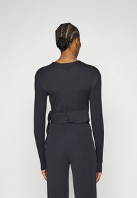 Fekete hosszú ujjú felső bordázott anyagból, rövidített szabással, derékrészen megkötővel. Sima textúra és testhezálló ujjak.