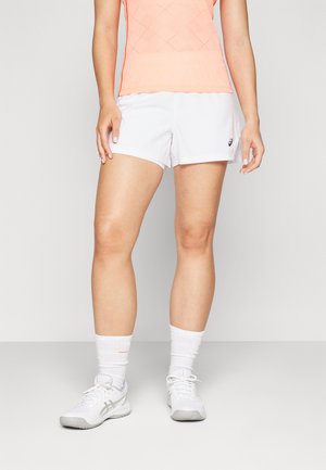 Witte sportshorts van lichtgewicht stof, met een gebogen zoom en een Asics-logo. Gecombineerd met een ademend perzikkleurig tanktop en witte sportschoenen.