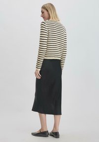 Gestreifter Strickpullover in Creme und Schwarz, kombiniert mit einem schwarzen Satin-Röhrenrock, knöchellang, und abgerundet mit schwarzen Ballerinas.