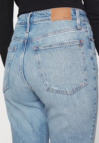 Vaqueros de tiro alto de color azul claro, hechos de denim, con costuras naranjas, dos bolsillos traseros y una etiqueta de cuero marrón en la cinturilla.