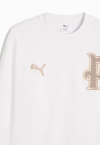Sweat-shirt blanc col rond avec logo Puma beige sur la poitrine gauche et grand patch en forme de lettre "P" stylisée sur la poitrine droite.
