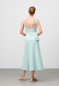 Mintgrön, utan ärmar topp med öppen rygg, i kombination med en matchande A-linjeformad midi kjol. Mjuk textur och enkel design, kompletterad med beige sneakers.
