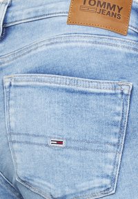 Vaaleansiniset farkut, joissa on takatasku, jossa on pieni punainen, valkoinen ja sininen logo. Nahkapinssi taskun yläpuolella, jossa on kohokuvioitu brändin nimi.