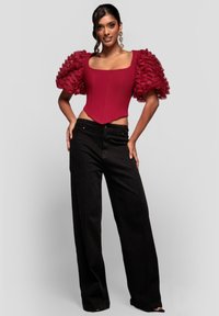 Rød bodystocking med puffede pufærmer med flæser, kombineret med højttaljede sorte bukser med vidde ben. Glat stof med struktureret pasform.