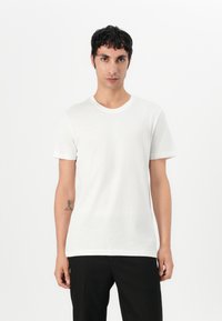 Tricou alb cu guler rotund, confecționat dintr-un material moale, având mâneci scurte și un tiv drept. Purtați cu pantaloni negri. Design minimalist.