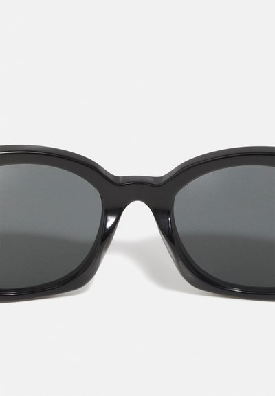 Óculos de sol pretos com armação de plástico brilhante, lentes planas e forma arredondada. Sem padrões visíveis ou detalhes de hardware.