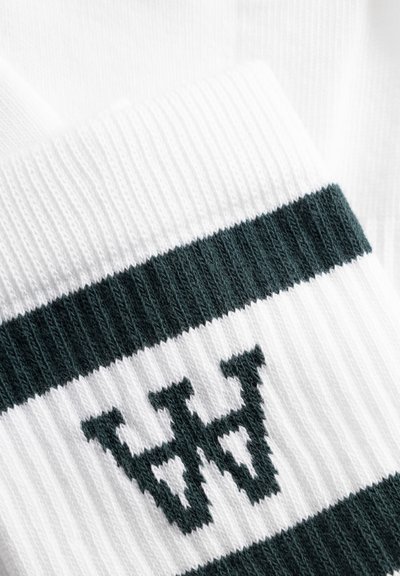 Tissu blanc côtelé avec deux rayures horizontales vert foncé et un "W" stylisé vert foncé tricoté entre les rayures.