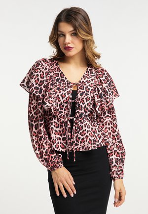 Frau trägt eine rosa-schwarze Leopardenprint-Langarmbluse mit Rüschen und Bindendetails, kombiniert mit einem schwarzen Rock.
