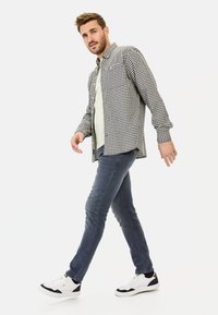Zwart-wit geruite shirt over een lichte top, gecombineerd met donkere jeans en witte sneakers met marineblauwe accenten.