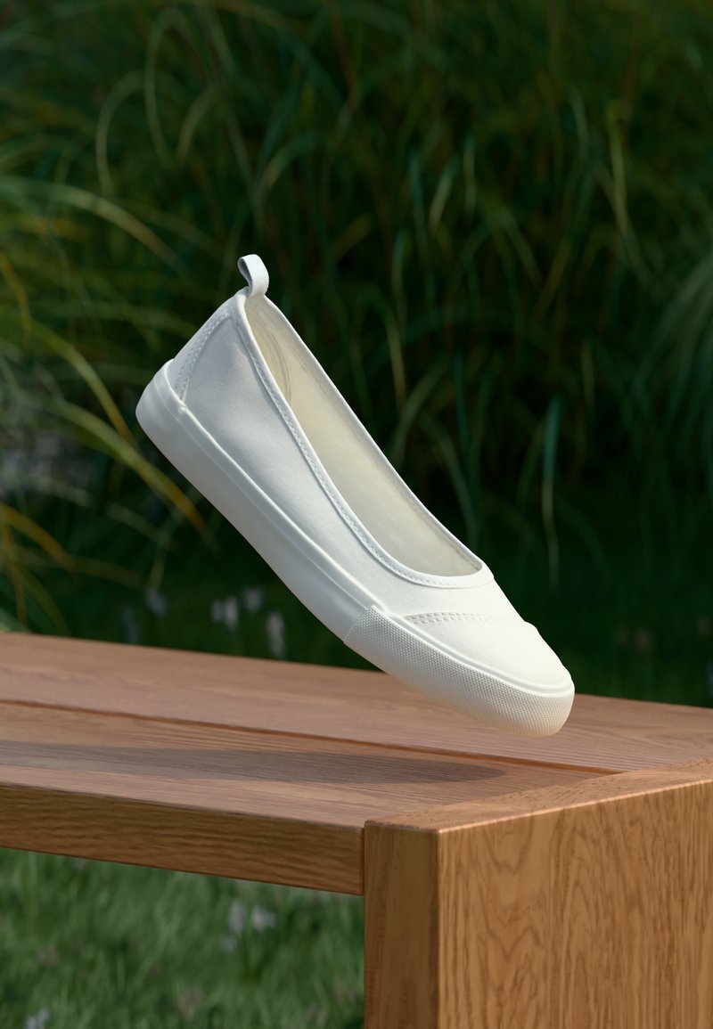 Chaussure en toile blanche à enfiler flottant au-dessus d'une table en bois en plein air, avec de l'herbe verte et des plantes en arrière-plan.