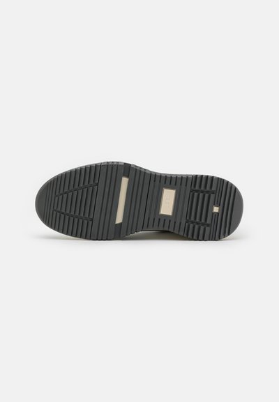 Black rubber shoe sole with textured grooves and ridges, featuring a cream-colored accent at the heel and a flat profile design.