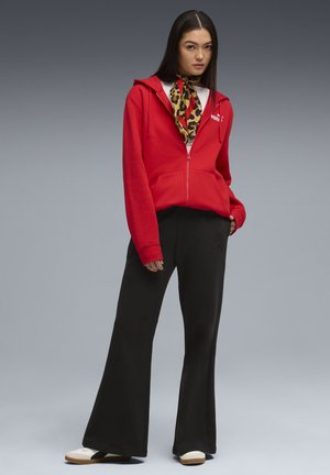 Rød zip-up hoodie med kengurulomme, sorte vide bukser og et leopardmønstret tørklæde. Hvide og sorte sneakers fuldender outfittet.