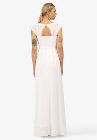 Witte maxi-jurk met kanten kapmouwen, een smock-bodice en een open rugdetail. Vloeiende, lichte stof die tot de grond hangt.