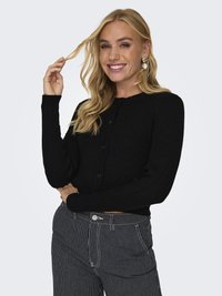 Schwarzer gerippter Cardigan mit rundem Ausschnitt, ausgestattet mit Knöpfen vorne und langen Ärmeln. Kombiniert mit schwarzen und weißen gestreiften Hosen.