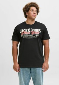 Crna pamučna majica s jakim bijelim i crvenim natpisom "JACK & JONES Denim Goods" s grafičkim detaljima na prednjoj strani. Standardni kroj.