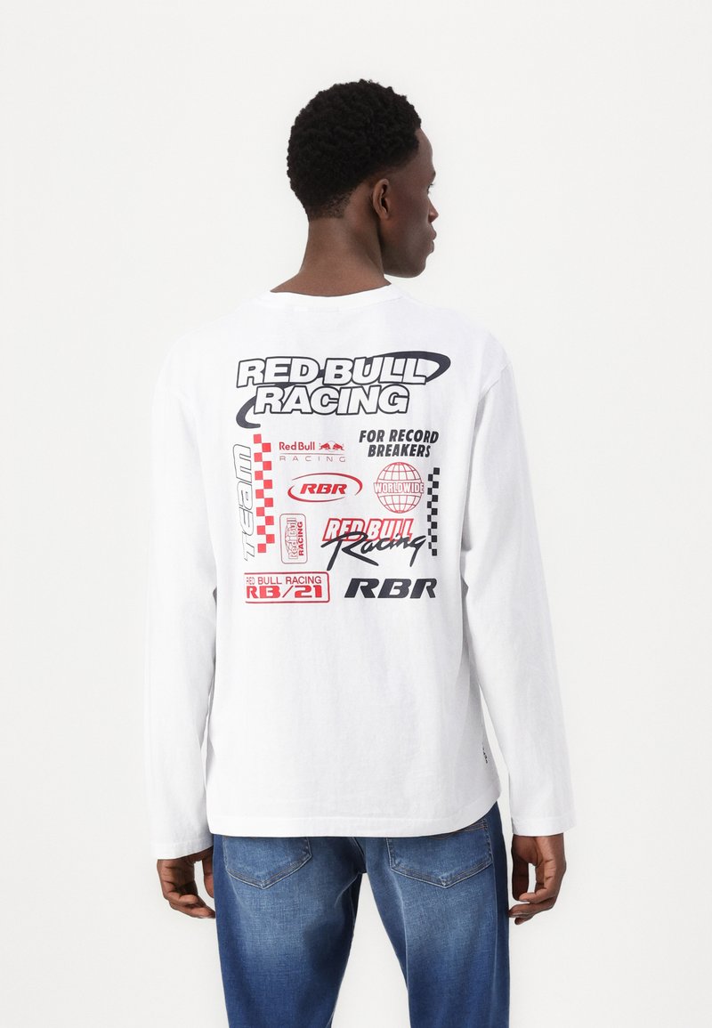 Bijela majica dugih rukava s grafičkim otiscima u crvenoj i crnoj boji, na kojoj se nalaze logotipi i tekst vezani uz Red Bull Racing na leđima.