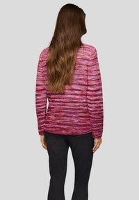 Gestrickter Pullover in Rosatönen mit einem strukturierten, mehrfarbigen Muster. Lange Ärmel und lockere Passform, kombiniert mit dunkler Hose.