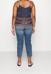Top sin mangas con estampado floral en color marino, con tirantes ajustables sujetos en los hombros, combinado con vaqueros de mezclilla azul claro y sandalias negras.