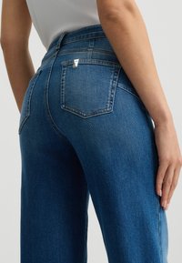 Hochgeschnittene blaue Jeans aus Denim mit geradem Bein, ausgestattet mit Gesäßtaschen, kontrastierenden Nähten und einem kleinen Markenlabel am Bund.