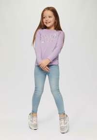 Lila pitkähihaine paita, jossa on "TALENT 2024" -kuvio, yhdistettynä vaaleansinisiin kapeisiin farkkuihin ja monivärisiin lenkkareihin. Sileä pinta.