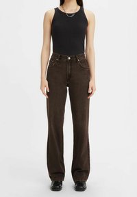 Top de tirantes negro acanalado combinado con unos vaqueros de pierna recta de tiro alto de color marrón oscuro, que cuentan con bolsillos en la parte delantera y una textura sutil. Botines negros.