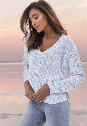 Helles blaues Strickpullover mit V-Ausschnitt, strukturiertem Muster, langen Ärmeln und gerippten Bündchen, kombiniert mit hellen Jeans.