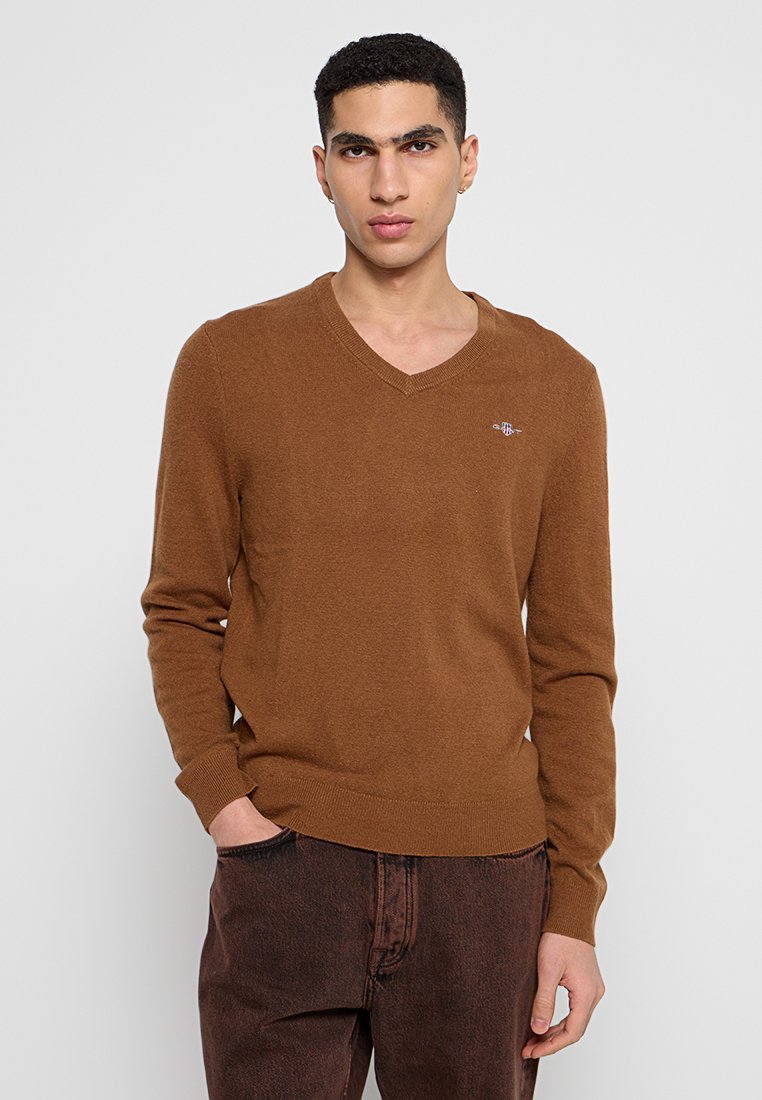 Brauner V-Ausschnitt-Pullover aus weichem Strickmaterial, mit gerippten Bündchen und Saum, subtiler Logo-Detail auf der Brust, lässige Passform.