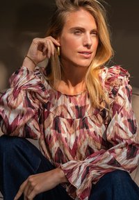 Kleurrijke, gestreepte blouse met gerimpelde mouwen in roze, wit en bruin tinten. Gemonteerd met donkere spijkerbroeken, heeft een ronde halslijn.