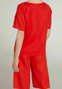 Rød linnedtop med korte ærmer og afslappet pasform, parret med matchende afskårne shorts. Glat tekstur og enkelt design.