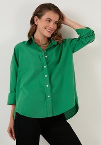Green button-up shirt in cotton blend, featuring a collar, long sleeves rolled at cuffs, a curved hem, and a relaxed fit.