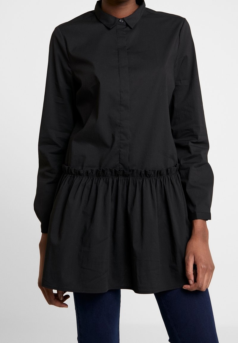 Chemise noire à boutons avec manches longues, un col et un détail de taille froncée. Fabriquée en tissu lisse, conçue pour une coupe décontractée.