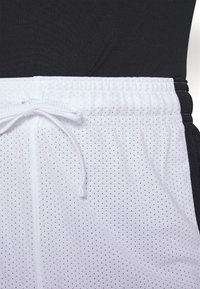 Vita mesh-idrottsshorts med en svart midjeband och sidodetaljer. Har en dragsnodd och en ventilerande textur.