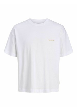 Adolescent portant une chemise à carreaux bleue boutonnée sur un t-shirt blanc, un short en denim gris, des chaussettes blanches et des baskets beige blanc, debout et souriant.