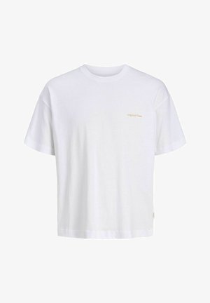 Adolescent portant une chemise à carreaux bleue boutonnée sur un t-shirt blanc, un short en denim gris, des chaussettes blanches et des baskets beige blanc, debout et souriant.