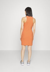 Vestido mini sem mangas laranja com silhueta ajustada, tecido texturizado e um simples detalhe de costura nas costas. Usado com sneakers prateados.