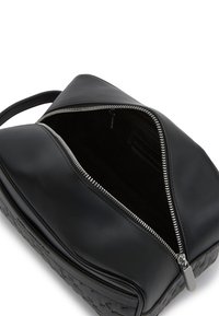 Svart lærveske med et teksturert, vevd mønster på den ene siden, med en sølvfarge glidelås som åpner til et romslig, mørkt interiør.