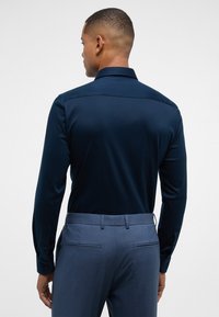 Marineblauwe longsleeve shirt met een gladde textuur, voorzien van een klassieke kraag en met knopen bij de manchetten, gecombineerd met lichtblauwe maatpakbroeken.