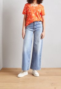 Orange blomstermønstret kortærmet t-shirt parret med højtsiddende, brede lyseblå jeans og hvide sneakers.