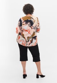 Blusa multicolorida con un patrón abstracto en tonos rosa, negro y marrón; presenta mangas de tres cuartos; combinada con pantalones negros hasta la rodilla y tacones.