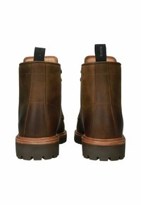 Botas de tobillo de cuero marrón con un acabado mate, que cuentan con una suela robusta, una entresuela de color marrón claro que contrasta y una lengüeta en la parte posterior.
