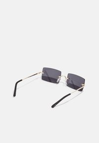 Sunglasses with rectangular dark lenses, thin gold metal frame, nose pads, and black plastic temple tips. Minimalist design.