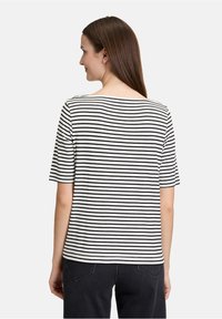 Sort og hvid stribet t-shirt med bred udskæring og korte ærmer, lavet af blødt stof, båret med sorte jeans.