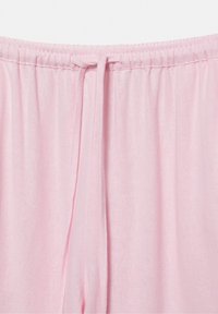 Světle růžové kalhoty s elastickým pasem a látkovým šňůrkem uvázaným vpředu uprostřed, vyrobené z měkkého, hladkého materiálu.