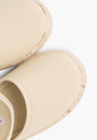 Chaussures en toile beiges à enfiler avec une surface texturée et un bord cousu. Semelle arrondie et design à talon ouvert pour une utilisation facile.